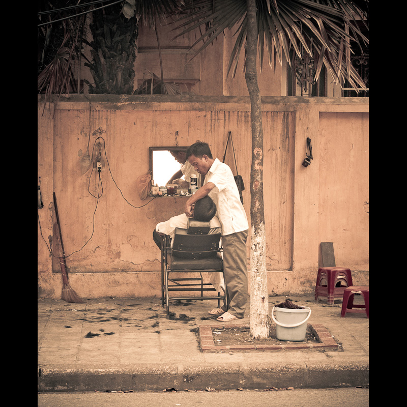 Asian man gets a haircut in the street of Hanoi